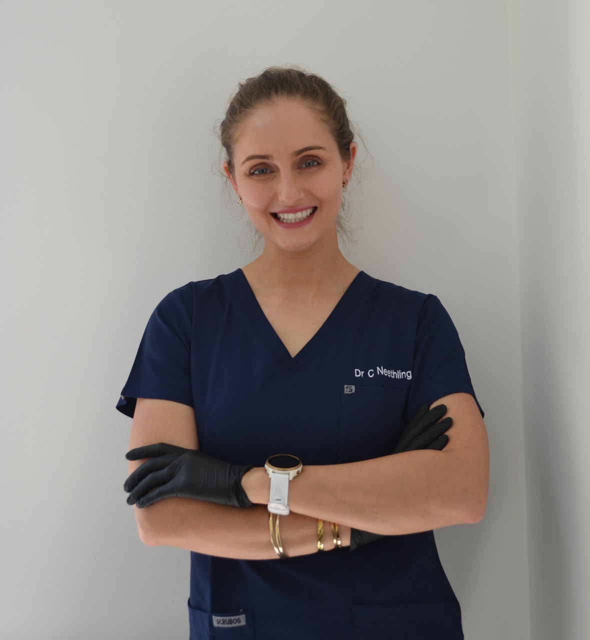 Dr Carlien Neethling in navy scrubs and black gloves, arms folded, smiling