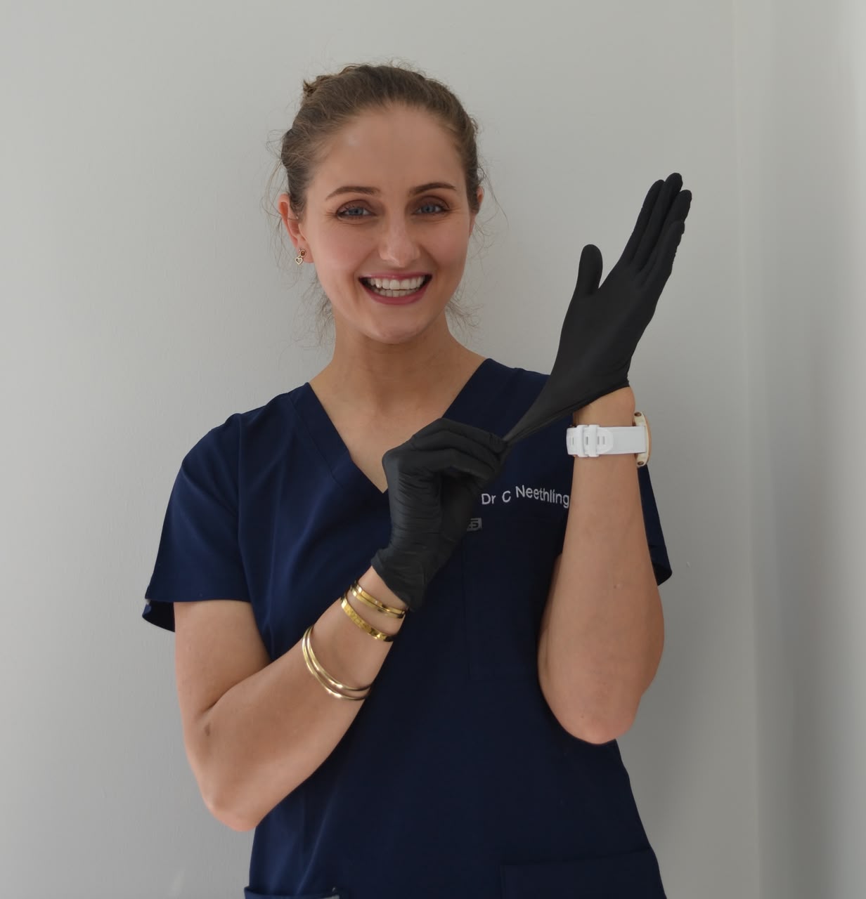 Dr Carlien Neethling in navy scrubs, smiling as she pulls on black gloves