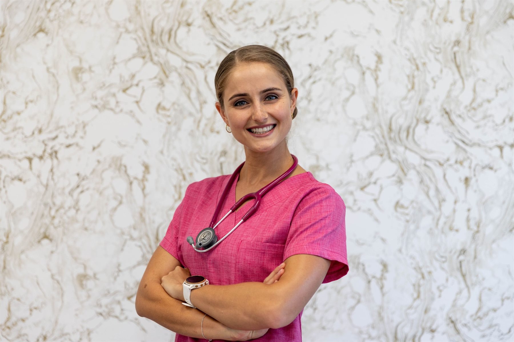 Dr Carlien Neethling in scrubs, arms folded, in front of a marble wall