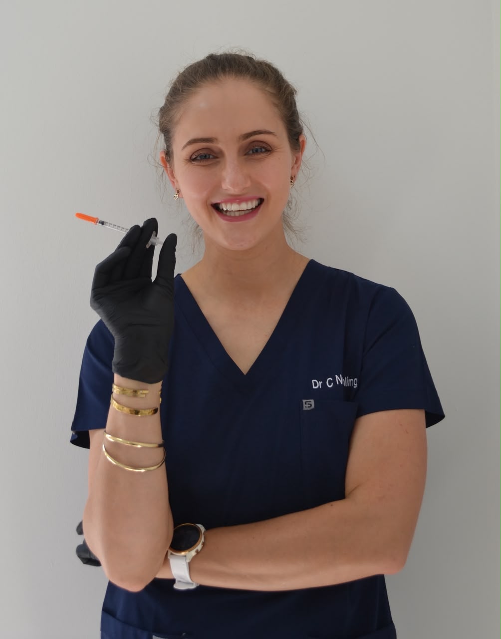 Dr Carlien Neethling smiling, holding a small syringe in a gloved hand